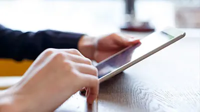 Man's hands holding a tablet on top of a table. 