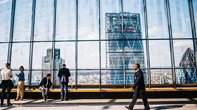 Five people hanging out in a hallway with floor to ceiling windows overlooking a city 